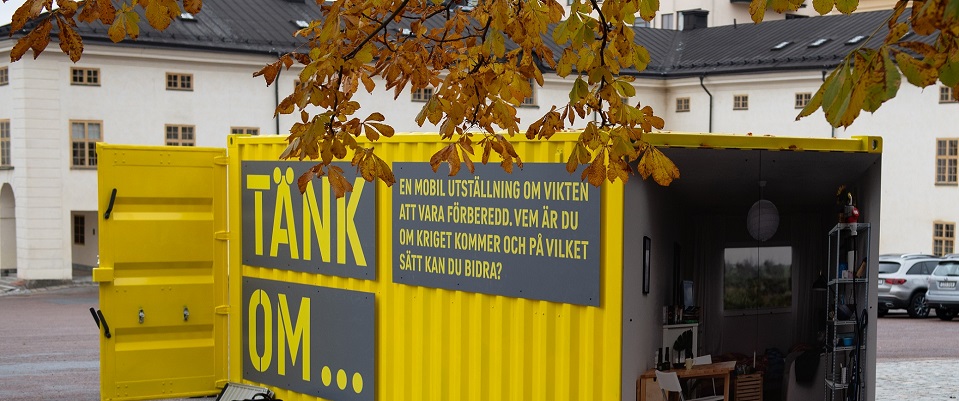 En knallgul container står på en kullerstenbelagd gård.